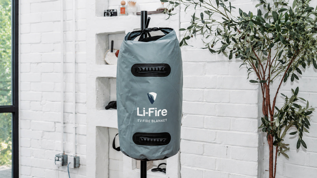 Li-Fire EV fire blanket in a gray carrying bag on a stand beside a potted tree in a loft studio.