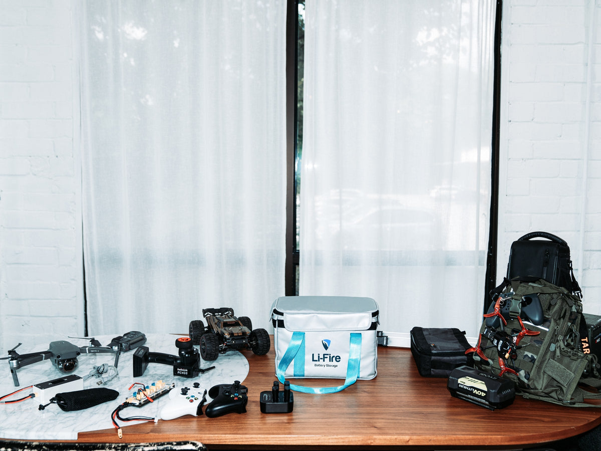 Li-Fire battery storage bag surrounded by drones, electronics, batteries, and equipment on a table.